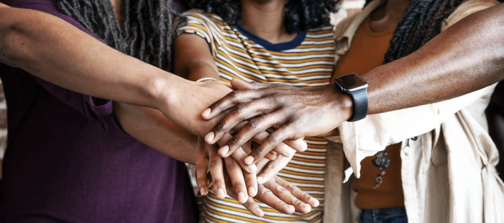 Diverse group stacks hands together in a gesture of unity